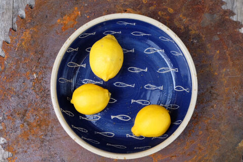 Dunkelblaue Schale mit weißem Fischdekor, darin drei Zitronen